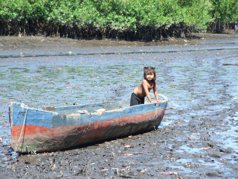 The neighbor girl playing in a boat on the mud flats waiting for the boys to return